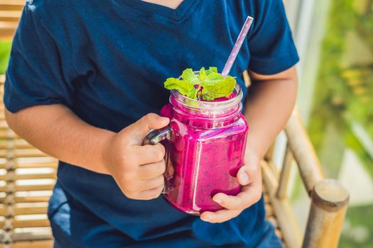 The boy holds smoothies from a dragon fruit with a mint leaf and a drinking straw.