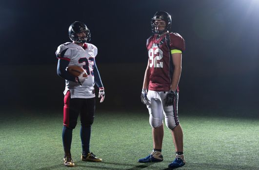 portrait of confident American football players holding ball while standing on field at night