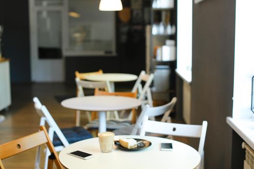 Empty cozy cafe with cups of coffe, smartphones and cake on table. Concept of interior and catering establishment, modern technology.