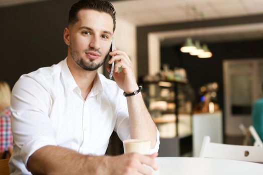 Young businessman talking by smartphone at cafe. Concept of modern technology and businessperson.