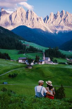 Santa Magdalena village in Val di Funes on the italian Dolomites. Autumnal view of the valley with colorful trees and Odle mountain group. Italy, man and woman on vacation, hiking in the mountains