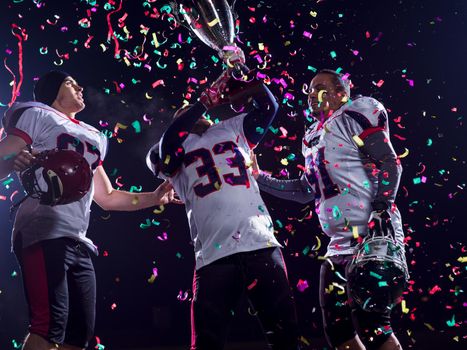 happy american football team celebrating victory with trophy and confetti on the night field