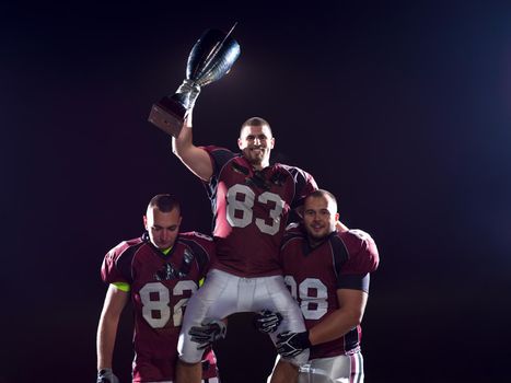 happy american football team with trophy celebrating victory on night field