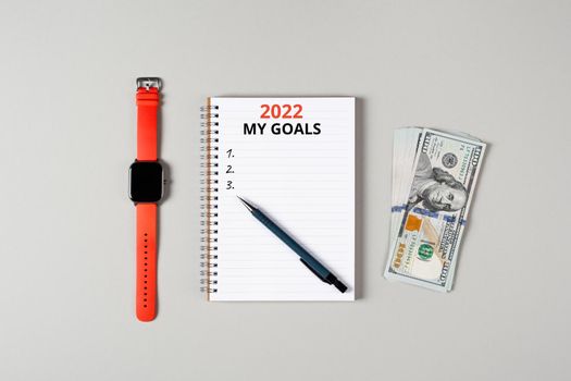 2022 my financial goals banner. Notepad, pen, stack of money and a cup of black coffee isolated on gray background. Notepad with copy space. Office, business, financial growth concept