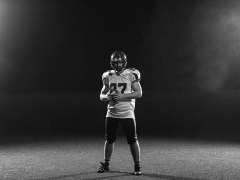 portrait of confident American football player holding ball while standing on field at night