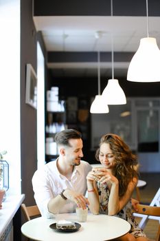 Young european husband hugging wife and sitting at cafe, drinking coffee. Concept of enjoing togetherness and having lunch.