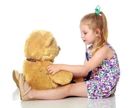 Beautiful little girl is playing doctor. She listens through a phonendoscope of a teddy bear. The concept of play and family happiness.