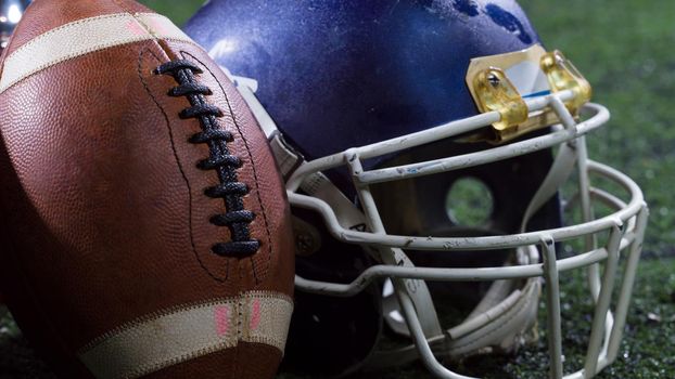 closeup shot of american football,helmets and trophy on grass field at night