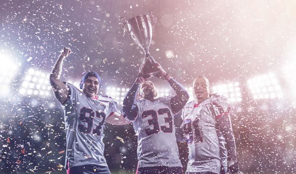 happy american football team with trophy celebrating victory in the cup final on big modern stadium with lights and flares at night