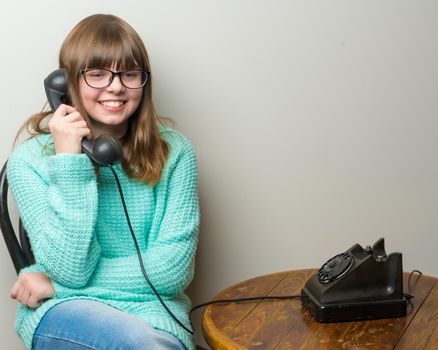 A beautiful little girl in a room in the fifties of the last century, talking on an old phone with a big black tube. Retro style. Concept of nostalgia, vintage.