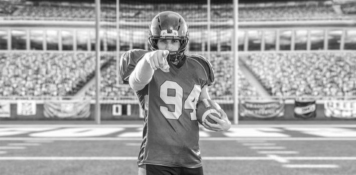 portrait of confident American football player holding ball while standing on field at night