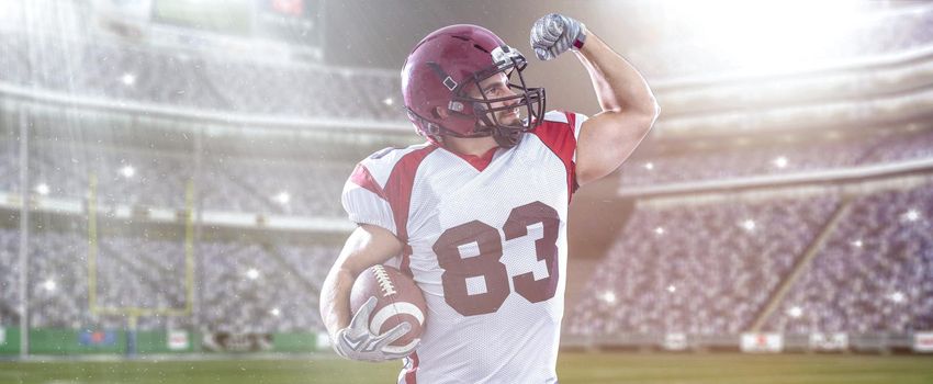 american football player celebrating touchdown on big modern stadium field with lights and flares