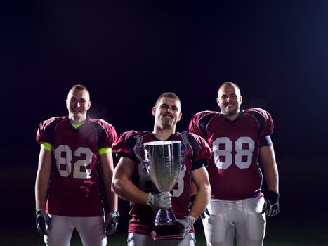 happy american football team with trophy celebrating victory on night field