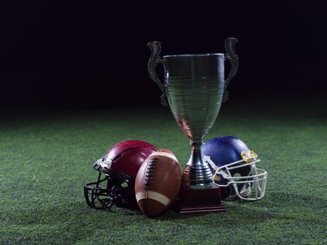 closeup shot of american football,helmets and trophy on grass field at night