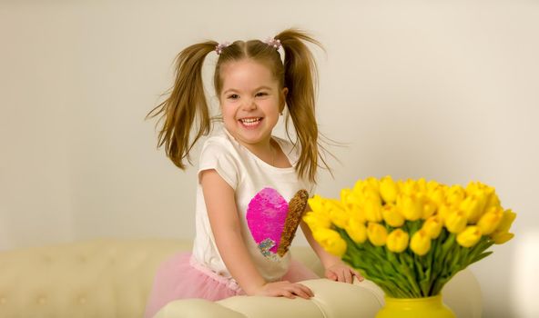 Happy little girl with a bouquet of flowers sitting on the couch. The concept of a holiday, a spring mood.