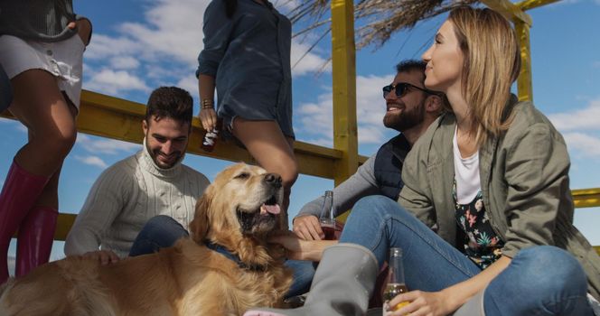 Happy Group Of Friends Hanging Out At Beach House having fun and drinking beer on autumn day