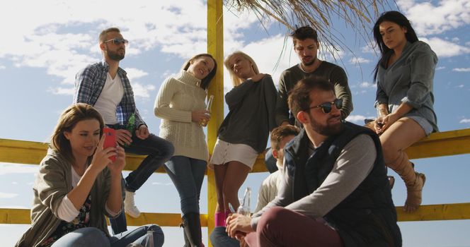 Happy Group Of Friends Hanging Out At Beach House having fun and drinking beer on autumn day