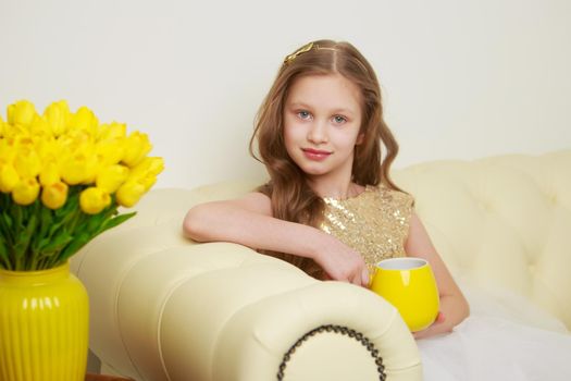 A cute little girl with a bouquet of tulips, in the spring in the studio. The concept of the awakening of nature after winter, the expectation of summer.