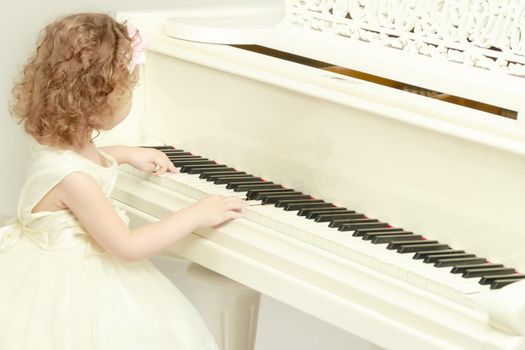 A nice little girl is playing on a big white piano. The concept of musical and aesthetic education of a child.