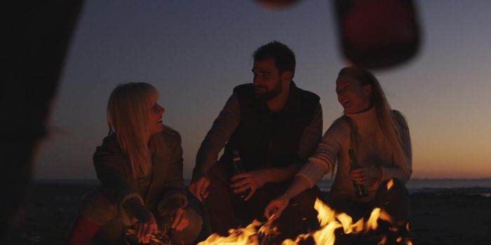 Group of young people having fun at beach around bonfire on sunset