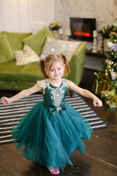 Little girl wearing blue dress standing near Christmas tree. Concept of celebrating New Year, fashion and childhood.