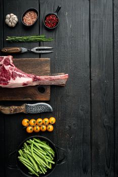 Cooking meat background. Raw tomahawk steak, with spices and herbs for cooking set, with grill ingredients, on black wooden table background, top view flat lay, with copy space for text