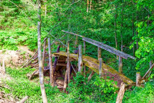 Old half-rotten wooden bridge covered with moss over a narrow stream. Long no longer used by humans. Kozionikha village, Kostroma region, Russia.