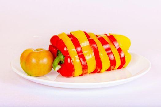 Sliced bell pepper red and yellow, and tomatoes are on a white plate. Healthy food concept.