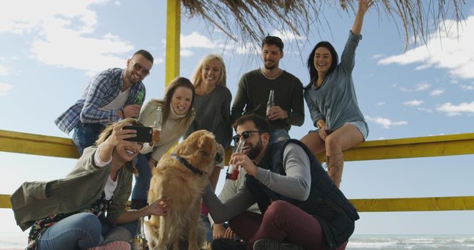 Happy Group Of Friends Hanging Out At Beach House having fun and drinking beer on autumn day