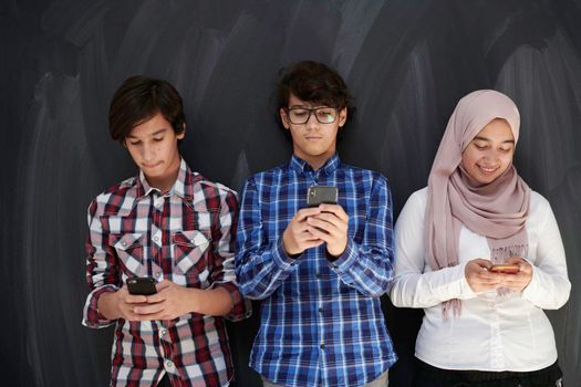 arab teenagers group using smart phones for social media networking against black chalkboard