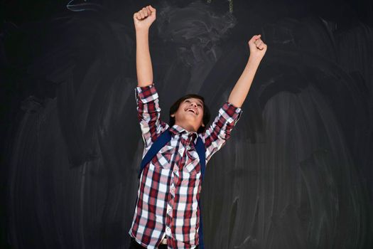 happy arab teenager celebrating wearing  backpack  casual school look against black chalkboard background