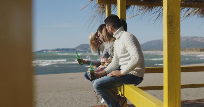 Happy Group Of Friends Hanging Out At Beach House having fun and drinking beer on autumn day