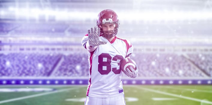 portrait of confident American football player holding ball while standing on field at night