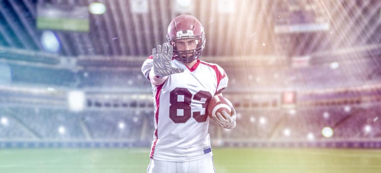 portrait of confident American football player holding ball while standing on field at night