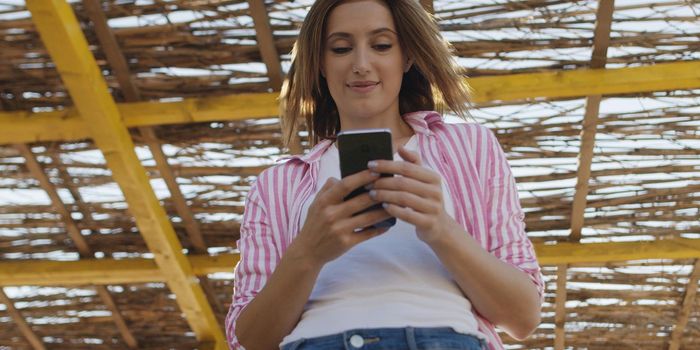 young woman using mobile cell smart phone app at beach during sunset on autumn day