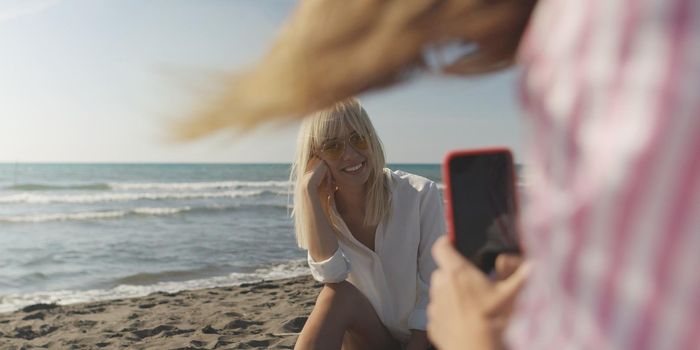 Two Girl Friends Taking Photo with Smartphone On Empty Beach during autumn day