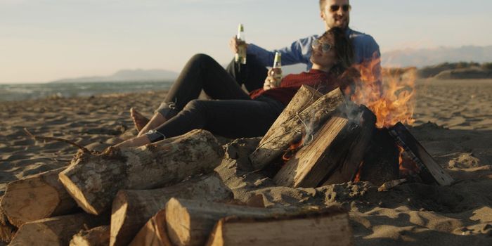 Young Couple Relaxing By The Fire, Drinking A Beer Or A Drink From The Bottle.