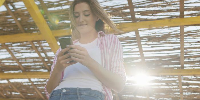 young woman using mobile cell smart phone app at beach during sunset on autumn day