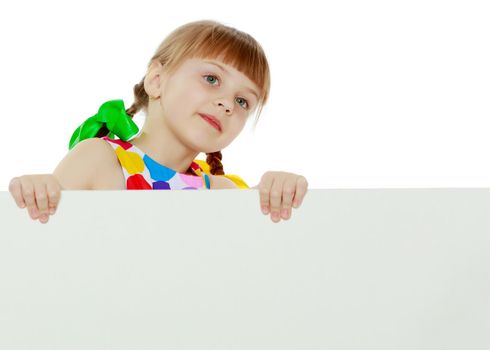 A beautiful Caucasian little blonde girl with long pigtails, in which large colored bows are braided, and a short bangs on her head. In a short summer dress.Looks because of the white obstacle.