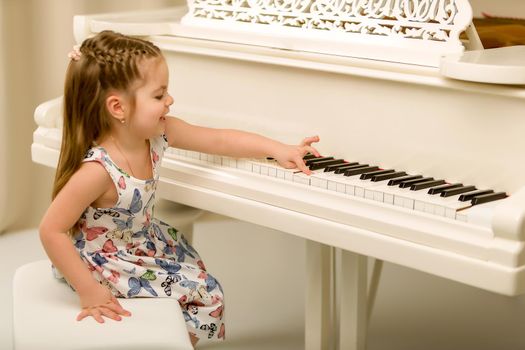 A nice little girl is playing on a big white piano. The concept of musical and aesthetic education of a child.