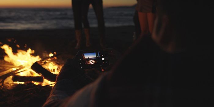 Boy Shows Girl A Picture On His Phone beside campfire on beach