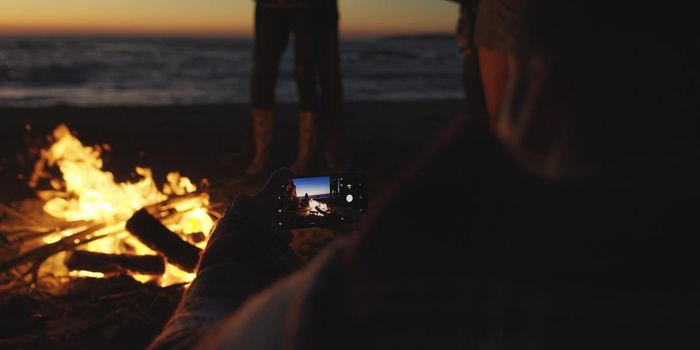 Boy Shows Girl A Picture On His Phone beside campfire on beach