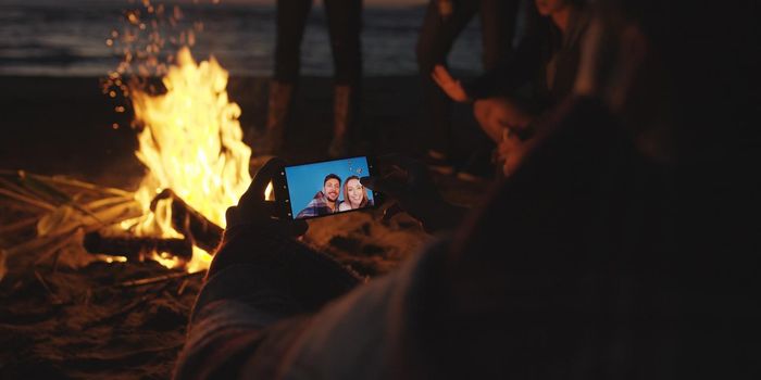 Boy Shows Girl A Picture On His Phone beside campfire on beach