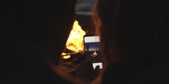 Boy Shows Girl A Picture On His Phone beside campfire on beach