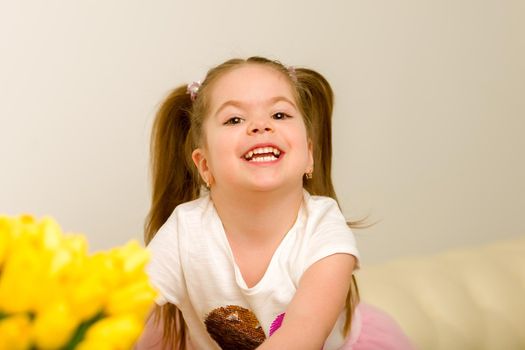 Happy little girl with a bouquet of flowers sitting on the couch. The concept of a holiday, a spring mood.