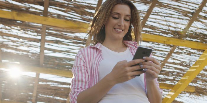 young woman using mobile cell smart phone app at beach during sunset on autumn day