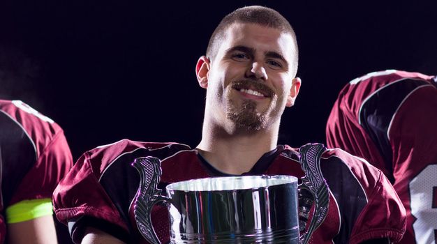 happy american football team with trophy celebrating victory on night field