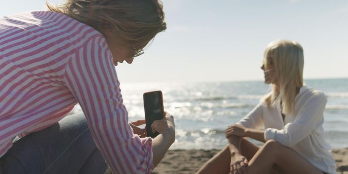 Two Girl Friends Taking Photo with Smartphone On Empty Beach during autumn day