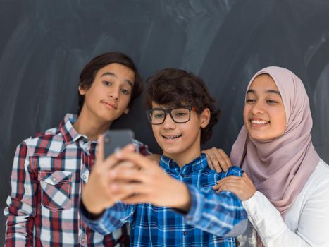 group of Arab teens taking selfie photos on smart phone with black chalkboard in background. High quality photo