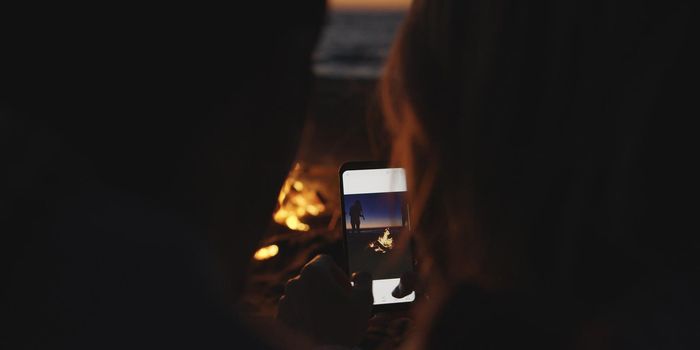 Boy Shows Girl A Picture On His Phone beside campfire on beach